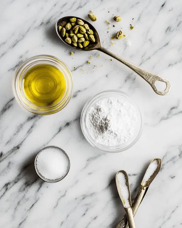 Pistachio Cream vs Butter: Ultimate Guide 2 Flat lay of pistachio cream ingredients including blanched pistachios, oil, salt, and powdered sugar on a marble countertop