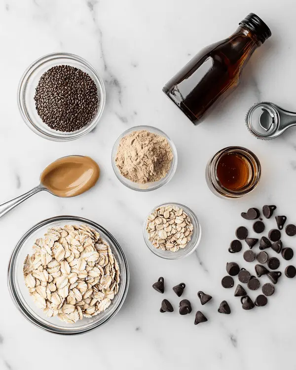 No Bake Lactation Cookies 2 Ingredients for no bake lactation cookies including oats, flaxseed, brewer's yeast, peanut butter, honey, vanilla, and chocolate chips arranged on marble counter