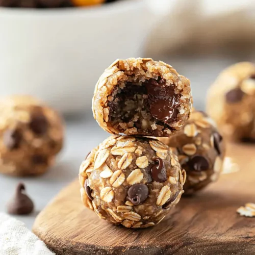 Stack of cookie balls no bake on wooden board with one cut in half showing oats, chocolate chips and M&Ms inside