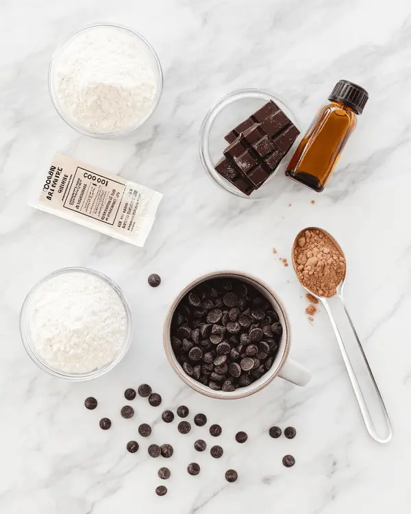 Hot Cocoa Mug Cake 2 Ingredients for hot cocoa mug cake arranged on marble countertop including flour, sugar, cocoa mix, baking powder, salt, hot water, oil, vanilla, and chocolate chips