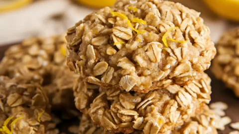 Stack of homemade lemon no bake oatmeal cookies on wooden cutting board with scattered oats and lemon zest
