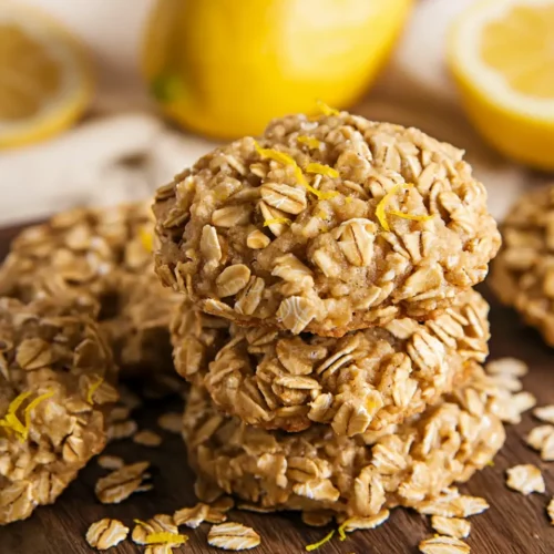 Stack of homemade lemon no bake oatmeal cookies on wooden cutting board with scattered oats and lemon zest