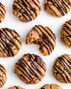 Professional photo of no-bake almond butter cookies with chocolate drizzle on white plate, one cookie broken to show texture
