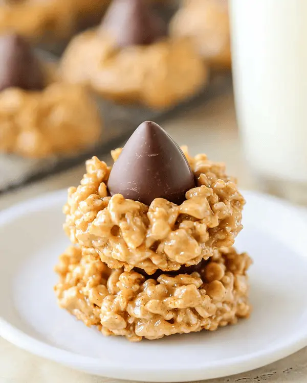 No Bake Peanut Butter Kiss Cookies 4 Stack of three no bake peanut butter kiss cookies on white plate next to glass of milk showing chocolate kisses and Rice Krispies texture
