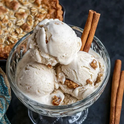 Three scoops of homemade oatmeal cream pie ice cream in glass bowl showing creamy texture and cookie pieces throughout